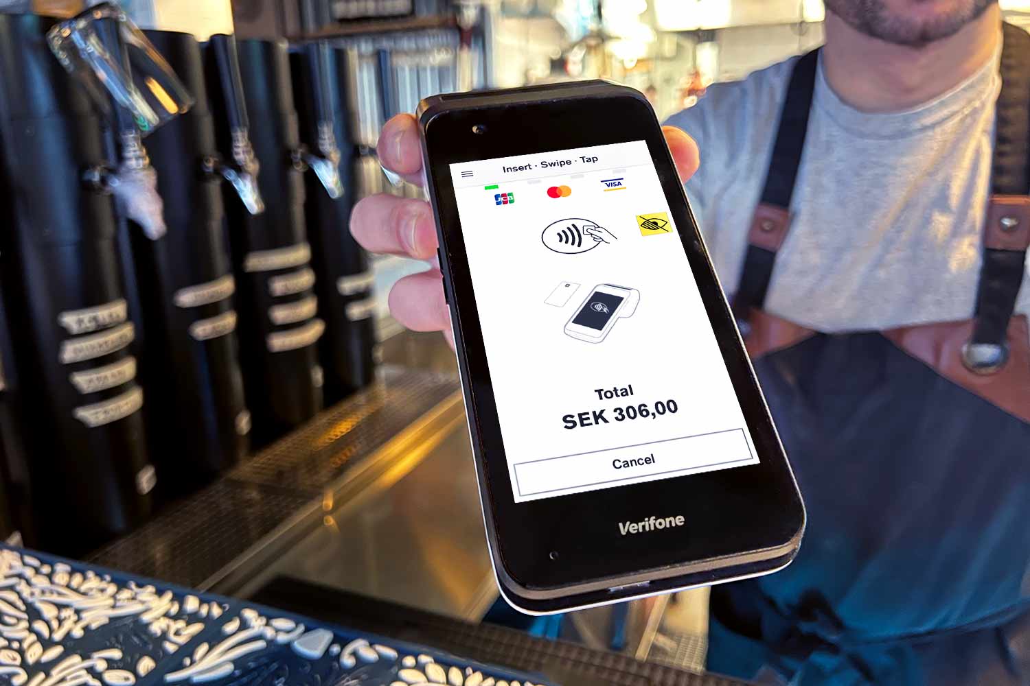 En servitör håller fram en Verifone CM5 med Onslip kassasystem installerad på och ska ta betalt över bardisken