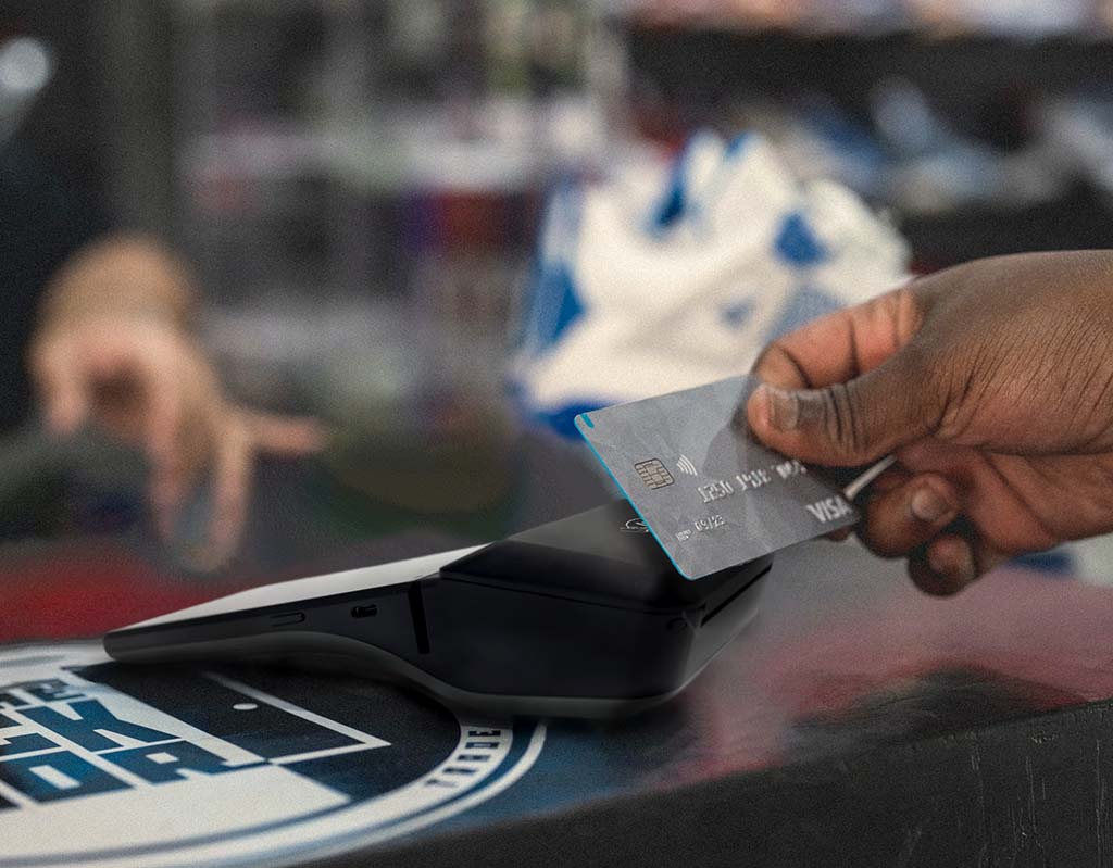 En person som betalar på en kortterminal med ett grått betalkort.