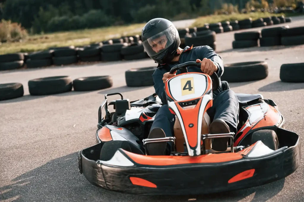 En person som kör gokart som har röda detaljer och svart stötfångare. I bakgrunden ser man däck som är utplacerade på asfalten för att skapa en gokartbana.