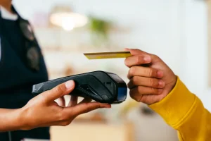 En person räcker fram en kortterminal till en person som håller ett betalkort ovanför kortterminalen och ska betal på betalsystemet